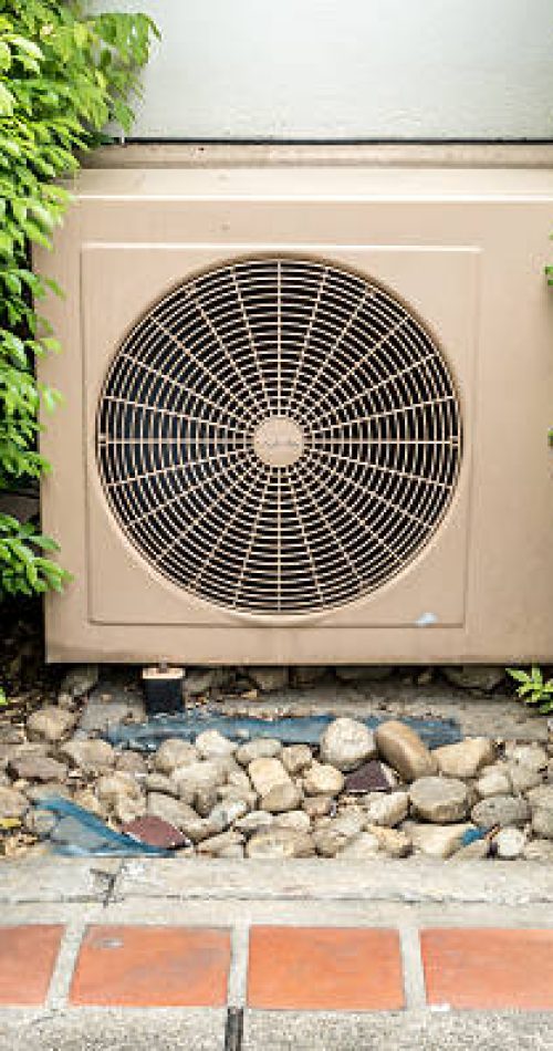 Side of air condition condenser unit between green leaves